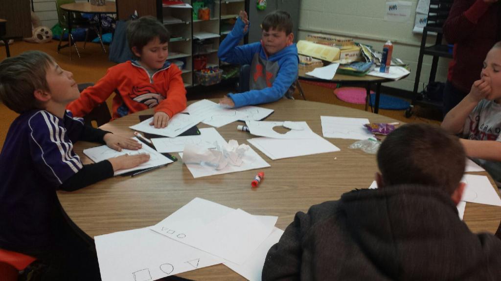 Five students sitting around the table exploring pictures with their eyes closed.